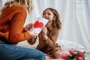 Red paper heart shaped present for, mother's day. Female parent with daughter is at home photo