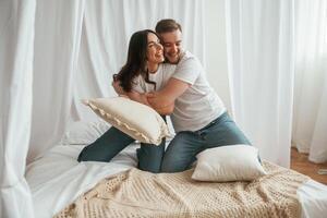 Soft ,pillows, are in hands, playing. Young couple are together at home photo