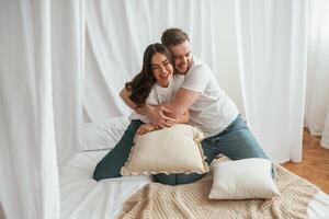Soft pillows, are ,in hands, playing. Young couple are together at home photo