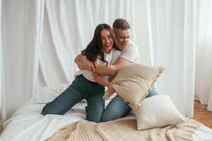 Soft, pillows are in hands, playing. Young couple are together at home photo