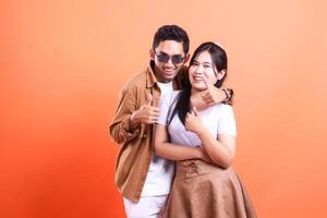 A couple poses happily showing a thumbs up gesture isolated on an orange background photo