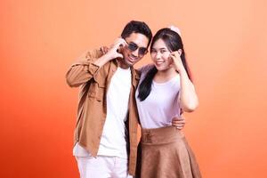 a pair of young lovers happy expression where the man stands and the woman hands sign love facing the camera romantic. isolated on orange background photo