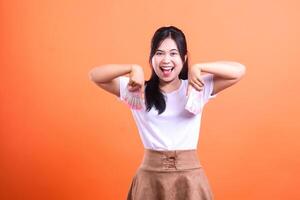 Woman with money in her hands smiling and pointing towards the ground on orange background photo