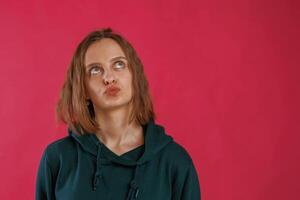 Making funny faces. Young woman is standing against red background in the studio photo