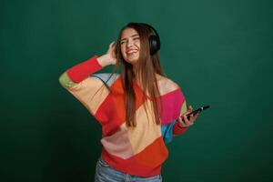 Feel the rhythm, listening to the music. Young woman is standing against green background in the studio photo