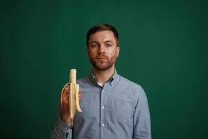 Holding banana. Man is standing against background in the studio photo