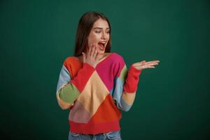 Showing by hand to ,the, side, place for text. Young woman is standing against green background in the studio photo
