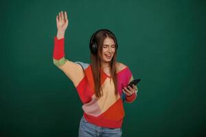 Feel,, the rhythm,, listening to the music. Young woman is standing against green background in the studio photo