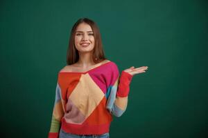 Showing by hand ,to ,the ,side, place for text. Young woman is standing against green background in the studio photo
