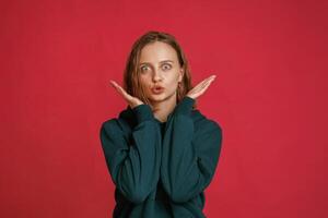 Making, funny faces. Young woman is standing against red background in the studio photo