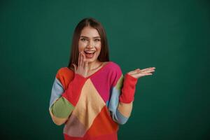 Showing ,by hand to the side, place for text. Young woman is standing against green background in the studio photo