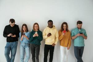 Busy, by using smartphones. Group of young people are standing against white background photo