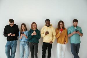 Busy by, using smartphones. Group of young people are standing against white background photo