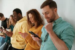 Busy by using, smartphones. Group of young people are standing against white background photo