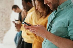 Side view. With smartphones, in hands. Group of young people are standing against white background photo
