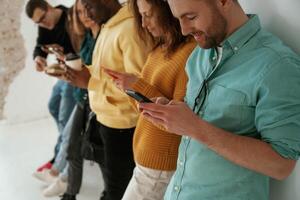 Side ,view. With smartphones in hands. Group of young people are standing against white background photo