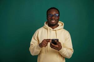 Using ,,smartphone. African, American man is standing against green background in the studio photo