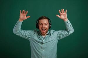 With hands up, in headphones. Man is standing against background in the studio photo