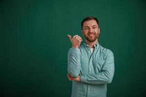 Showing to the side by finger to the empty space for text. Man is standing against background in the studio photo