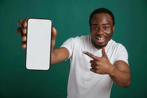 Smartphone with, white empty space for text. African American man is standing against green background in the studio photo