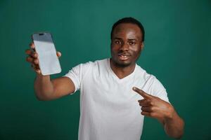 Smartphone with white ,empty space for text. African American man is standing against green background in the studio photo