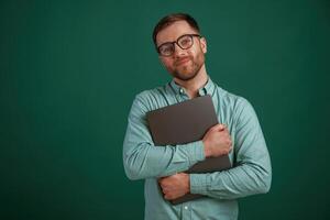 Silver colored laptop in hands.. Man is standing against background in the studio photo