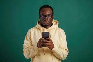 Using smartphone.. African ,American man is standing against green background in the studio photo
