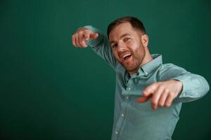 Pointing finger, smiling. Man is standing against background in the studio photo