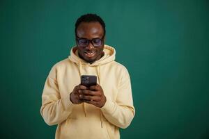 Using ,smartphone. African American man is standing against green background in the studio photo
