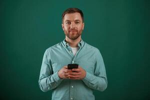 Black, smartphone in hands. Man is standing against background in the studio photo