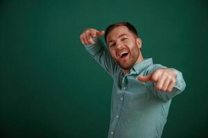 Pointing, finger, smiling. Man is standing against background in the studio photo