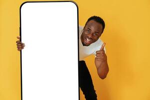 With,, very ,big smartphone for copy space.. Black man is in the studio against yellow background photo
