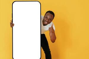 With very big smartphone, for copy, space. Black man is in the studio against yellow background photo