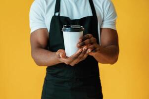 Coffee in hands, worker. Black, man, is in the studio against yellow background photo