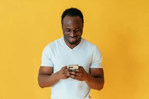 Holding smartphone and smiling. Black man is in the studio against yellow background photo