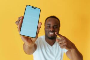 Blue ,colored ,,smartphone for copy space in hand. Black man is in the studio against yellow background photo