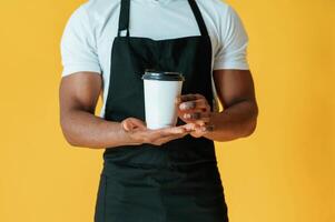 Coffee in,, hands,, worker. Black man is in the studio against yellow background photo