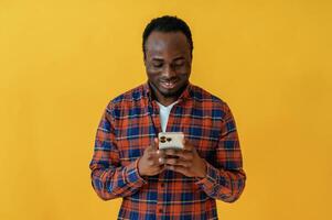 Smiling and holding smartphone. Black man is in the studio against yellow background photo