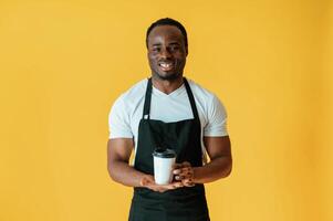 Coffee in hands, worker... Black man is in the studio against yellow background photo