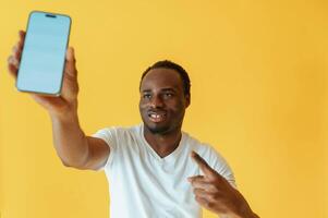 Empty, display of smartphone, holding.. Black man is in the studio against yellow background photo