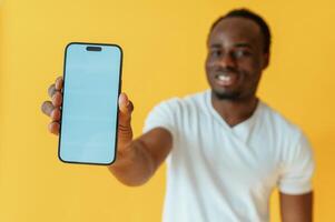 Blue ,colored smartphone for copy space in hand. Black man is in the studio against yellow background photo