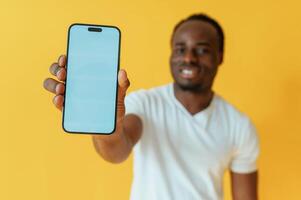 Blue colored smartphone, for copy space in hand. Black man is in the studio against yellow background photo