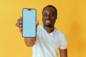 Blue colored, smartphone for copy space in hand. Black man is in the studio against yellow background photo