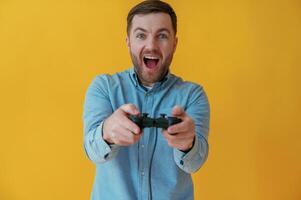 Playing game with, joystick. Attractive man in blue shirt is against yellow background photo