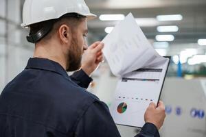 Turning the pages of documents... Factory worker is indoors with hard hat photo