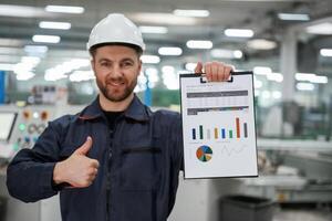 Plan ,with graphs in hand... Factory worker is indoors with hard hat photo