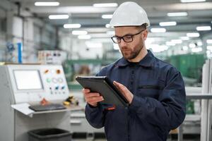 Holding ,tablet. Factory worker,, is ,indoors with hard hat photo