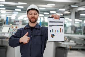 Plan, with ,graphs ,in hand. Factory worker is indoors with hard hat photo