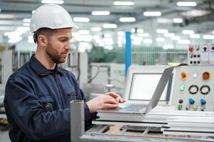Using,, the laptop. Factory, worker is indoors with hard hat photo