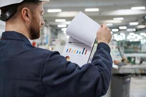 Turning, the, pages of documents. Factory, worker is indoors with hard hat photo